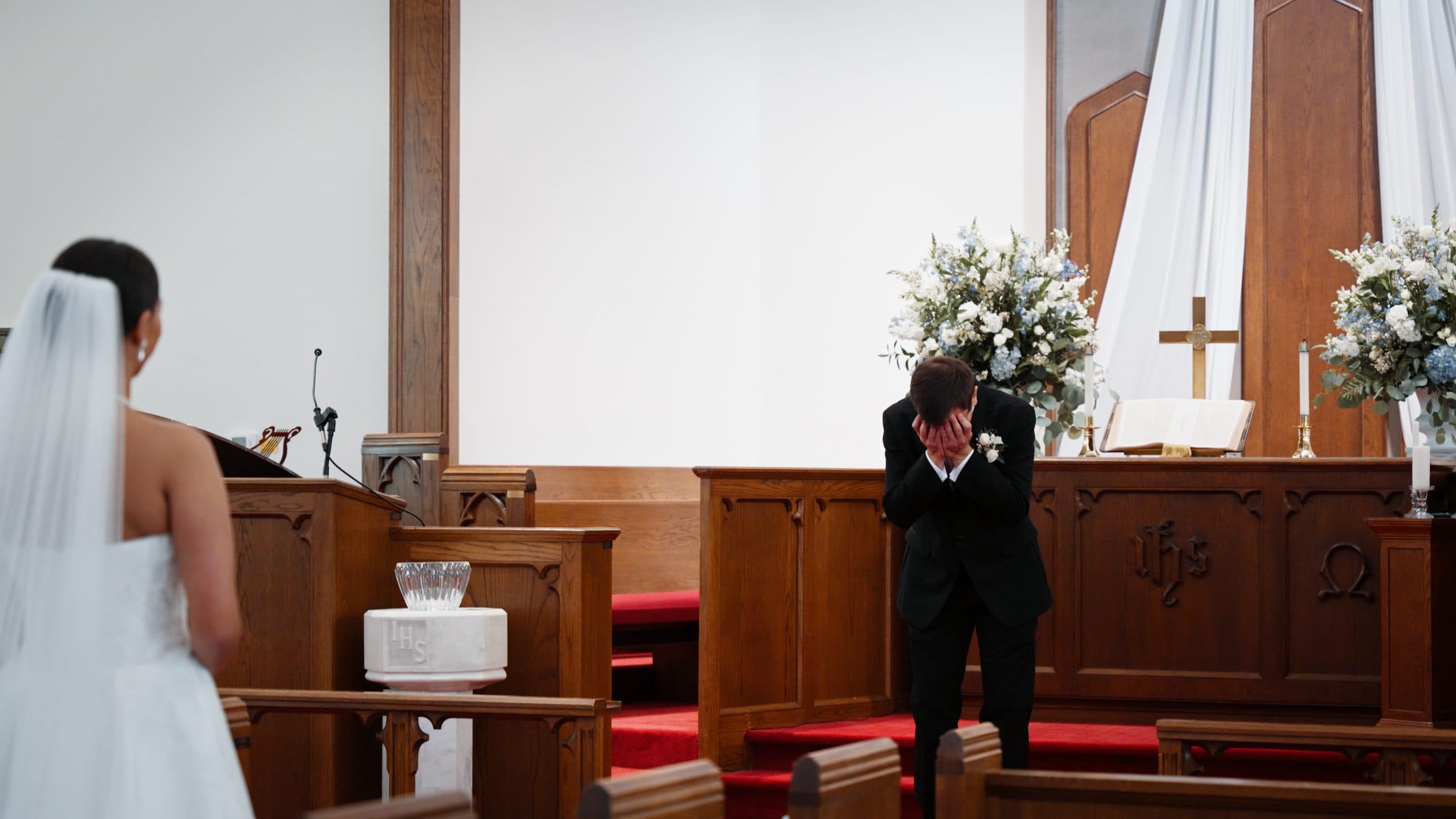 A groom at the altar, wiping his eyes as the doors open